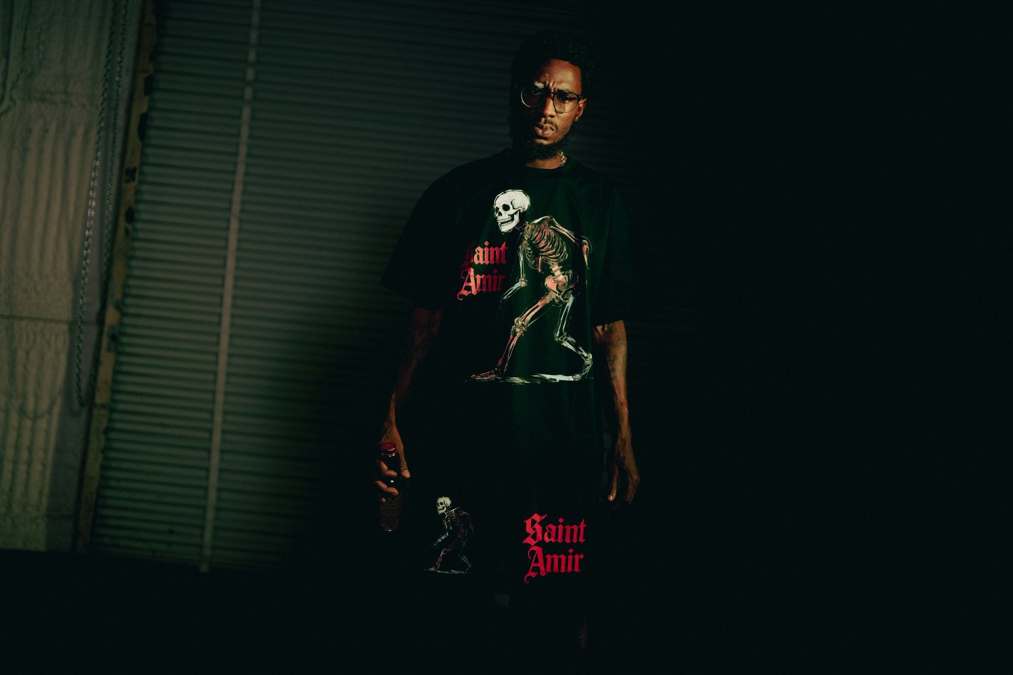 Person wearing a dark t-shirt with graphic designs and text in a dimly lit room.